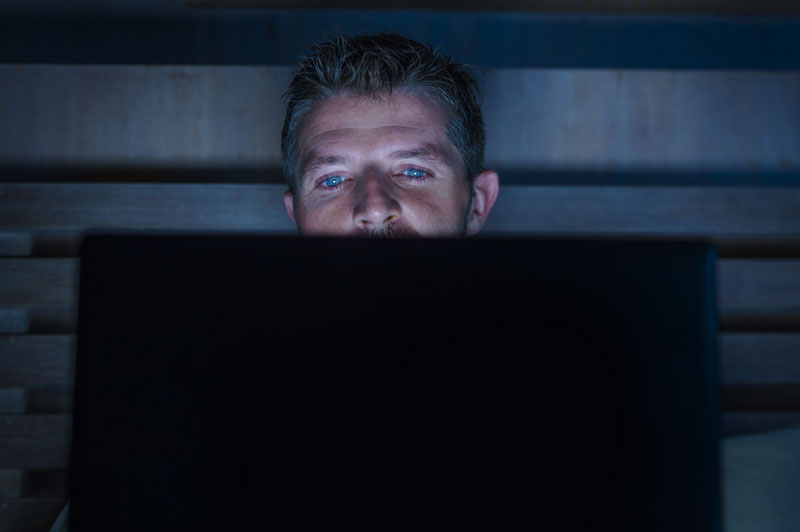 Mies katsoo pimeässä tietokoneen ruutua.